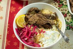 a bowl filled with meat, rice and veggies on top of a table