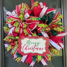 a christmas wreath on the front door decorated with red, green and white ribbons that say merry christmas