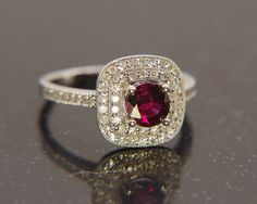 a close up of a ring with a red stone in the center and diamonds around it