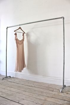 a dress hanging on a clothes rail in an empty room with wood flooring and white walls