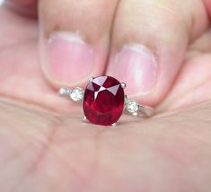 a close up of a person holding a ring with a red stone