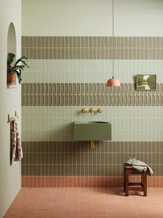 a bathroom with a green sink and brown tiled wall next to a wooden stool on the floor