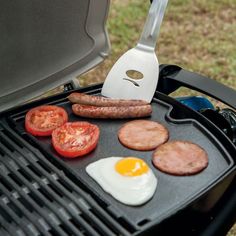 sausages, eggs and tomatoes are cooking on a bbq with a spatula