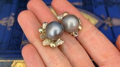 These gorgeous pearl earrings are each accented with one (1), post set, cultured Tahitian pearl, eleven (11), bead set, round brilliant cut diamonds and two (2), prong set, baguette cut diamonds. The earrings measure 22.8mm X 17.3mm. The earrings are finished with hinged omega backs for pierced ears. One of the baguette diamonds is unnoticeably chipped. Tahitian Pearl Jewelry With Diamond Accents For Wedding, Tahitian Pearl Jewelry With Matching Earrings For Anniversary, Classic Tahitian Pearl Earrings For Anniversary, Elegant Tahitian Pearl Earrings For Anniversary, Elegant Tahitian Pearl Earrings For Wedding, Elegant Tahitian Pearl Jewelry For Anniversary, Tahitian Pearl Round Earrings For Wedding, Round Tahitian Pearl Earrings For Wedding, Luxury Tahitian Pearl Earrings For Anniversary