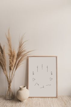 a white vase sitting next to a plant on top of a wooden table in front of a framed photograph