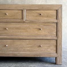 a wooden dresser with three drawers and two knobs on the front, sitting against a white wall