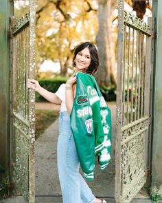 a woman standing in an open gate with a green scarf around her neck and jeans on