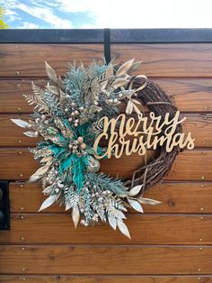 a wreath with the word merry christmas hanging on a wooden wall next to a mailbox