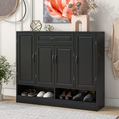 a black cabinet with two doors and shoes on it in front of a wall painting