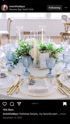 the table is set with blue and white dishes, silverware, candles, and greenery