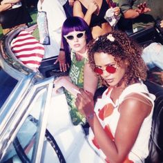 two young women sitting in the back of a convertible car at an outdoor music festival