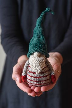 a person holding a small knitted christmas ornament in their hands, wearing a green hat