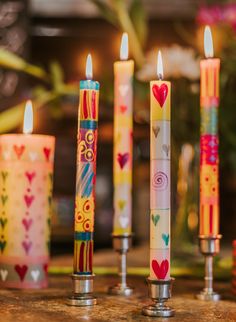 four candles with hearts painted on them sitting next to each other in front of a vase