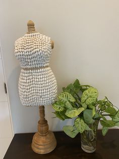 a vase filled with green plants next to a mannequin on top of a table