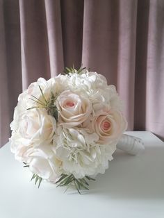 a bouquet of white and pink flowers sitting on top of a table next to a curtain