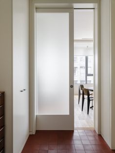 an open door leading to a dining room table and chairs in the background with red tiles on the floor