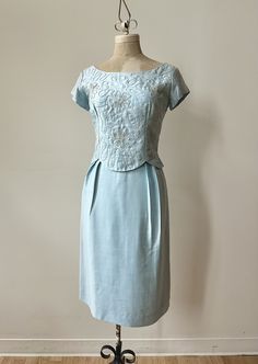 "A sweet and simple baby blue '60s number by 'Matinee' of Canada.  Classic sheath style dress with a darling overlay bodice that has a scalloped peplum bottom and swirling white embroidery that flows into the occasional flower pattern.  Fully lined and fastens up the center back with the original metal zipper and in pristine condition with no flaws to note.  ~ Measurements ~  Bust: 36\" snug Waist: 26\" Hip: 36\" Bodice Length: 15\" Skirt Length: 25.5\"" Fitted Blue Vintage Dress For Wedding, Blue Fitted Vintage Dress For Vintage Occasions, Fitted Blue 1950s Style Dress, Light Blue Fitted Vintage Dress For Spring, Blue 1950s Fitted Vintage Dress, Elegant Vintage Blue Dress With Fitted Bodice, Elegant Blue Vintage Dress With Fitted Bodice, Formal Fitted Vintage Blue Dress, Vintage Fitted Dress For Mother Of The Bride