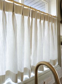 a kitchen window with white curtains hanging from it's side and a gold faucet next to it