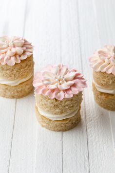 three cupcakes with frosting and pink flowers on them sitting on a white surface