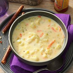 a bowl of soup with carrots, cauliflower and bread sticks on the side