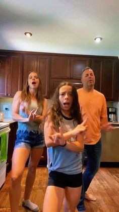 three people are standing in a kitchen and one person is holding out her hand to the other