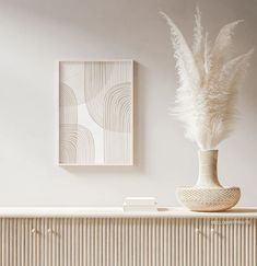 a white vase sitting on top of a wooden table next to a wall mounted art piece