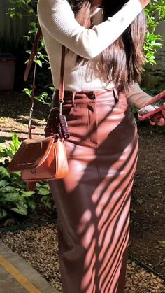 a woman in a long skirt is holding a cell phone and looking into the distance