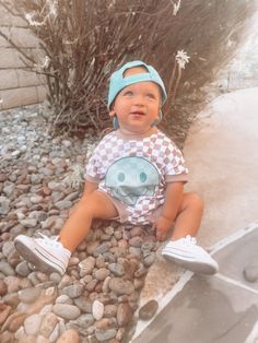 a small child sitting on some rocks and wearing a blue hat with a smiley face