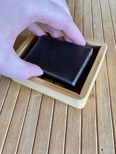 a person is placing something in a small wooden box on the floor with their hand