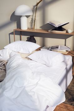 a bed with white sheets and pillows next to a lamp on a wooden shelf above it