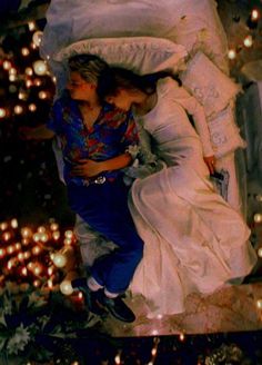 two people laying on top of a bed covered in lights