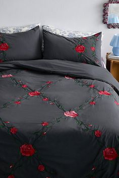 a bed with grey sheets and red roses on the comforter is in front of a mirror