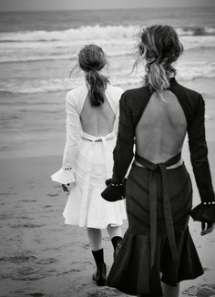 two women walking on the beach with their backs to each other, back to back