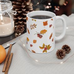 a coffee mug with autumn leaves on it next to some cinnamon sticks and an orange