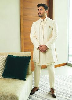 a man standing in front of a couch wearing a white sherve with green pillows