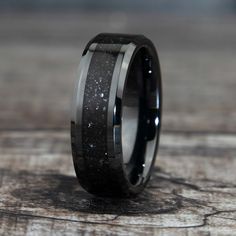 a black and silver wedding ring with wood inlays on the inside, sitting on a wooden surface