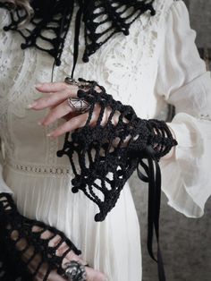 a close up of a person wearing a white dress and black crochet gloves