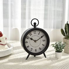 an alarm clock sitting on top of a table next to a cake and potted plant