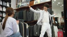 a young man is standing in front of a clothing rack and talking to a woman