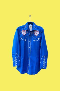 Vintage H Bar C Ranchwear Royal Flush Shirt  The real deal! This style shirt was originally worn by the card dealers at the Frontier Hotel in Las Vegas in the late 1950s - it was an instant hit! Own a fantastic piece of vintage history - this shirt is in excellent preowned condition.  No stains, tears, fading or obvious blemishes.   Item tag reads: H Bar C Ranchwear.  California Ranchwear.  Made in USA.  Eldorado Collection.  Size 14-1/2.  Royal Flush Length: ~30" Chest Circumference (pit to pit): ~39" 100% polyester Famous royal flush cards applique Multicolor chain stitching, smile pockets, rodeo cuffs and pearl snaps.   AMAZING Please examine photos carefully.  This shop does not accept returns/exchanges/refunds on vintage items. Western Blue Button-up Top, Blue Western Shirt With Button Closure, Classic Blue Tops For Rodeo, Blue Rodeo Top With Snap Buttons, Blue Snap Button Tops For Rodeo, Blue Snap Button Top For Rodeo, Blue Fitted Western Tops, Blue Tops With Snap Buttons For Rodeo, Fitted Blue Western Tops