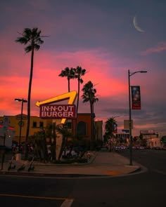 a restaurant with palm trees in the foreground and a pink sky behind it at sunset