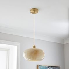 a light fixture hanging from the ceiling in a living room with white walls and paintings on the wall