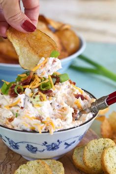 a hand dipping a cracker into a bowl of potato salad with bacon and cheese