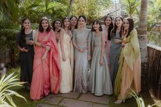 a group of women standing next to each other in front of some trees and plants