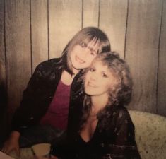 two women sitting next to each other in front of a wooden wall with planks