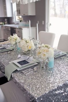 the table is set with silver sequins and white flowers