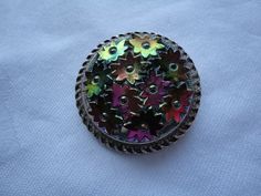 "A rare and unusual vintage pale gold tone and Carnival glass scarf clip/ring dating from the 1940's. The carnival glass is shaped in to pretty flowers in shades of purple and green surrounded by ornate pale gold tone border. It measures approx 1.25\" diameter. In excellent vintage condition with a good strong, tight clip. Postage in the UK is by Royal Mail First Class Signed For service. Postage to all other countries is by Royal Mail Airmail Tracked and Signed For service." Vintage Multicolor Round Brooches, Vintage Multicolor Collectible Brooches, Vintage Brooches With Decorative Buttons As Gift, Vintage Brooches As A Gift With Decorative Buttons, Vintage Multicolor Brooches, Vintage Silver Pins For Party, Vintage Multicolor Wedding Brooches, Vintage Multicolor Brooch For Party, Multicolor Vintage Brooch For Party