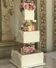 three tiered wedding cake with pink and purple flowers on the top, sitting on a table in front of a mirror