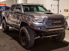 a gray toyota truck parked in a showroom with people looking at the trucks on display