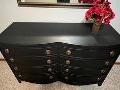 a black dresser with flowers on top in front of a mirror and a framed picture